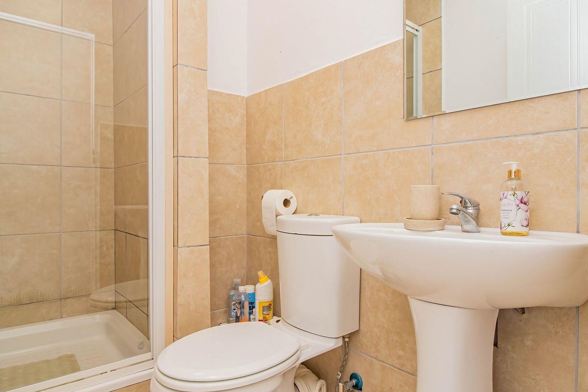 A functional bathroom featuring a shower enclosure, pedestal basin, and toilet with neutral ceramic wall tiling.