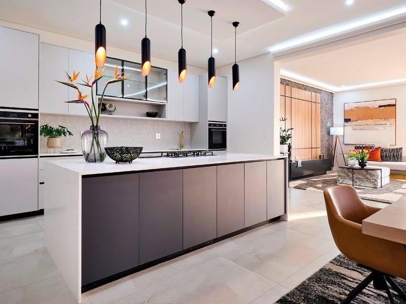 Modern open-plan kitchen featuring a large central island, sleek cabinetry, built-in appliances, and stylish pendant lighting, seamlessly flowing into the living area.