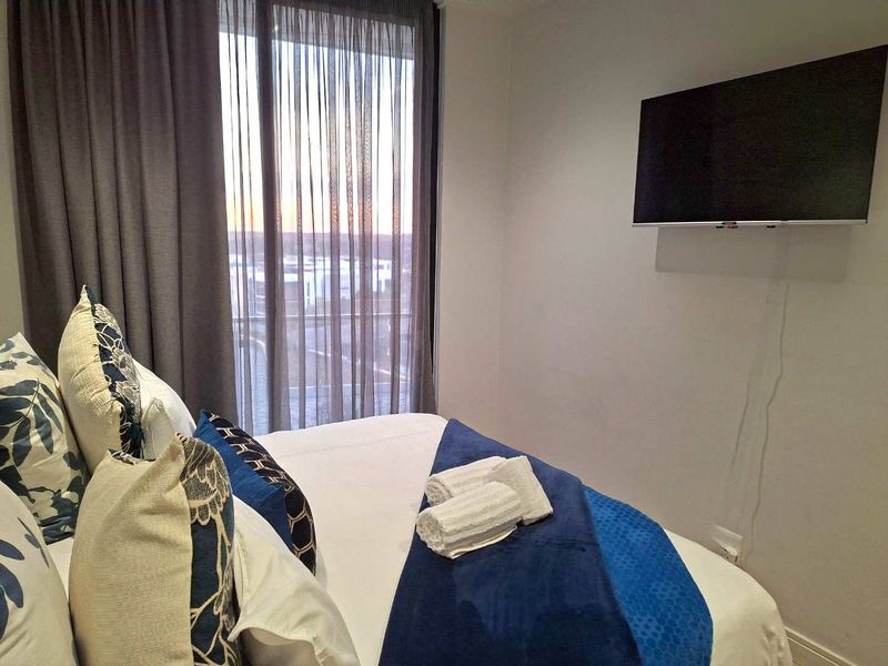 A well-maintained bedroom featuring a large sliding glass door with curtains and a wall-mounted television, offering a clean and functional living space.