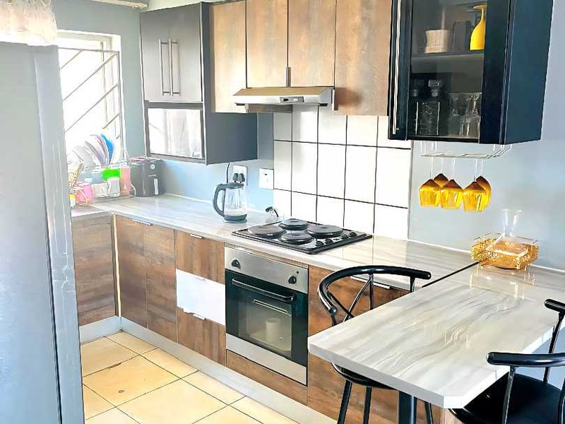 Functional kitchen featuring wood-look cabinetry, built-in oven and hob, tiled backsplash, and an integrated breakfast bar for casual dining.