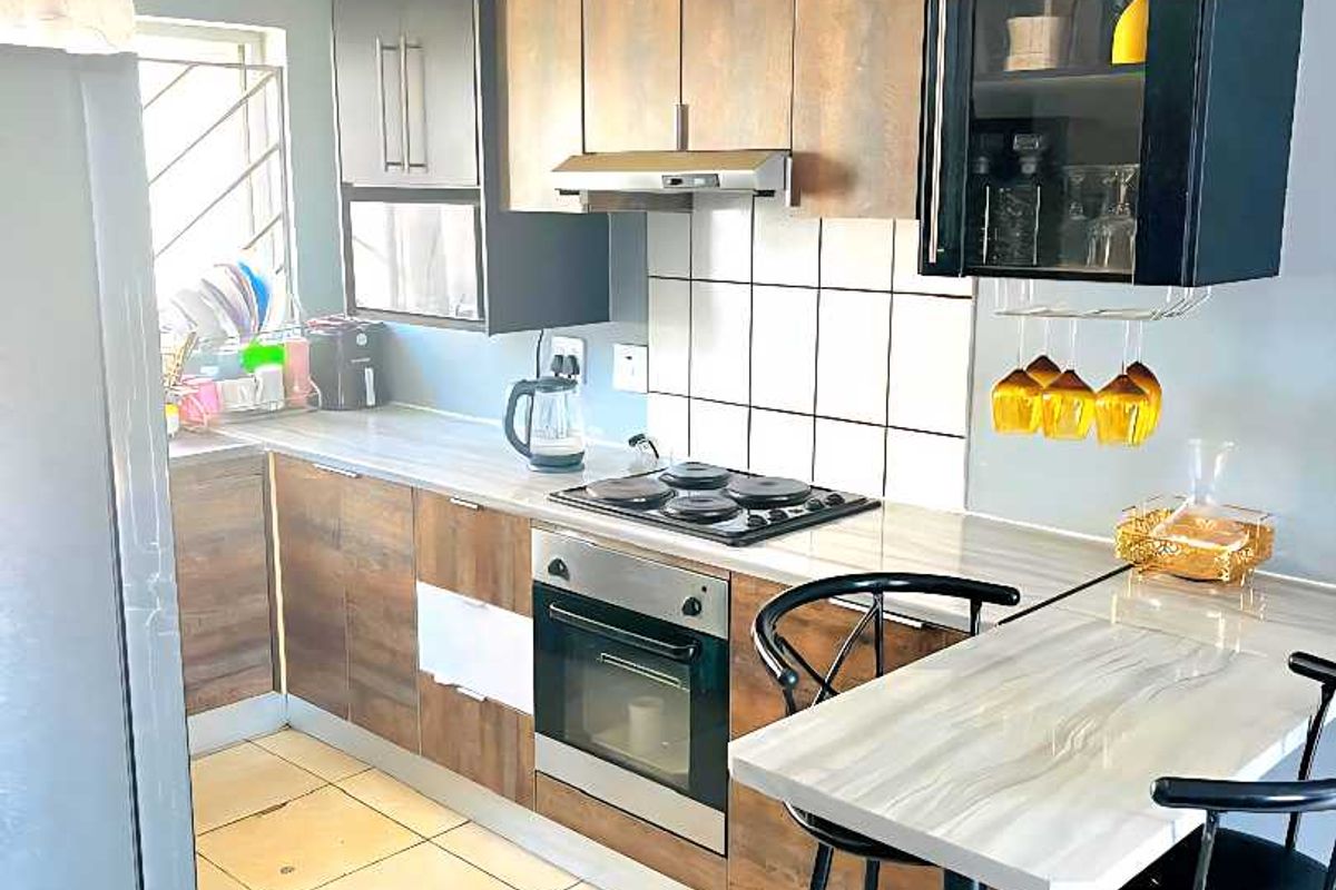Functional kitchen featuring wood-look cabinetry, built-in oven and hob, tiled backsplash, and an integrated breakfast bar for casual dining.