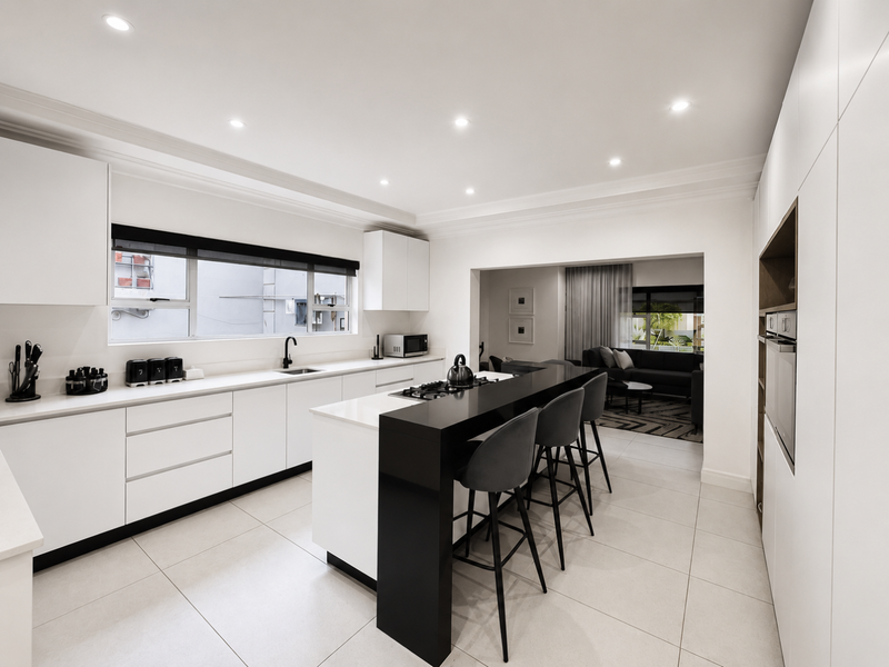 Modern open-plan kitchen featuring sleek white cabinetry, a contrasting black island with breakfast bar, stone countertops, and integrated appliances.
