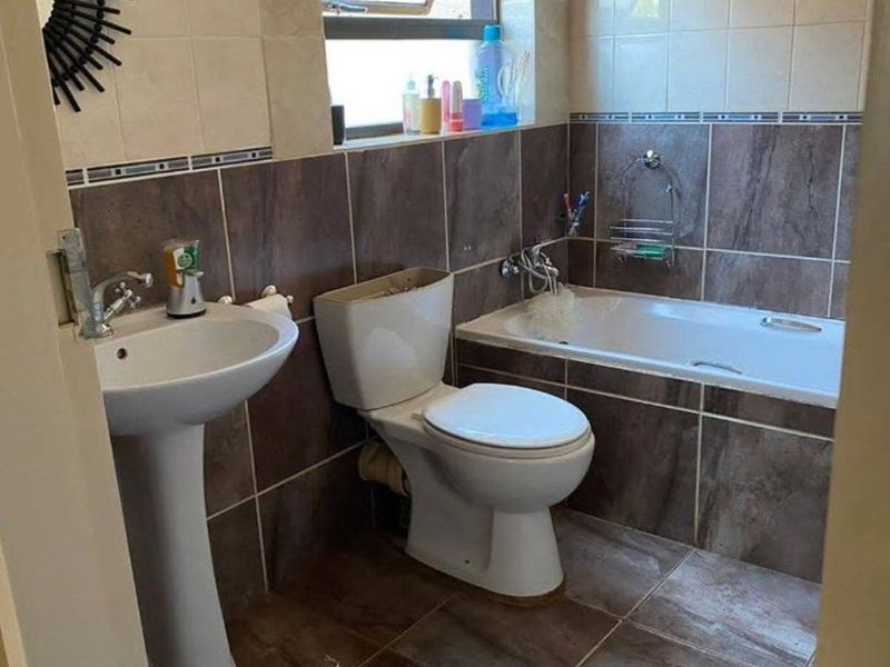 A functional bathroom featuring a pedestal basin, toilet, and a built-in bathtub with tiled finishes throughout.
