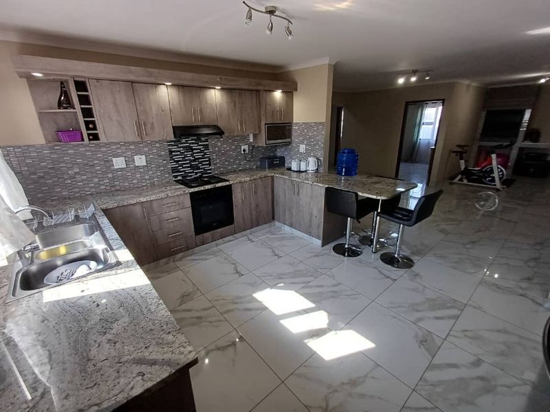 Modern open-plan kitchen featuring granite countertops, wood-finish cabinetry, tiled flooring, and integrated appliances, flowing seamlessly into the adjacent living area.