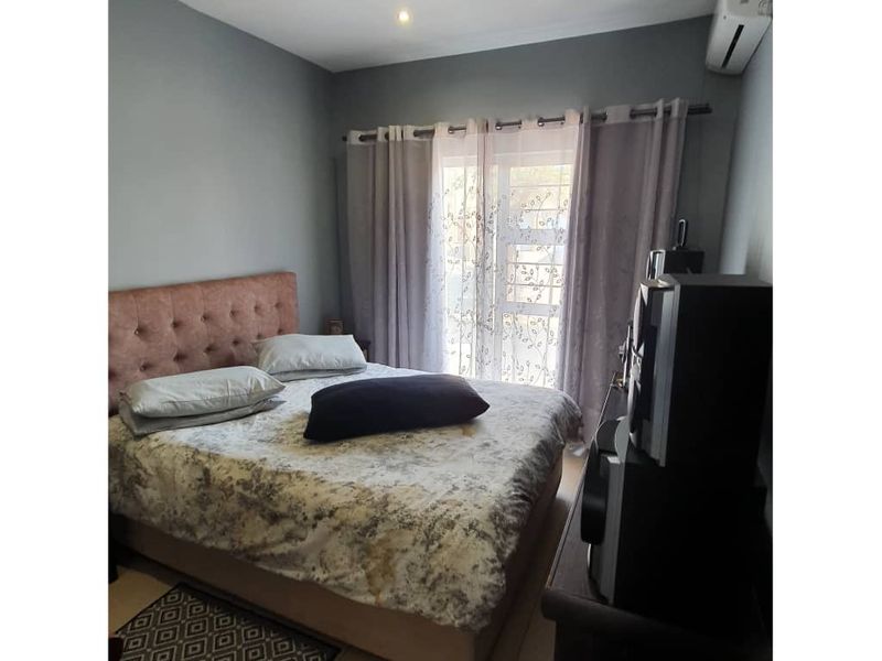 A well-maintained bedroom featuring tiled flooring, a wall-mounted air conditioning unit, and a sliding glass door providing natural light.