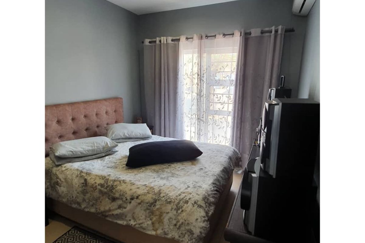 A well-maintained bedroom featuring tiled flooring, a wall-mounted air conditioning unit, and a sliding glass door providing natural light.