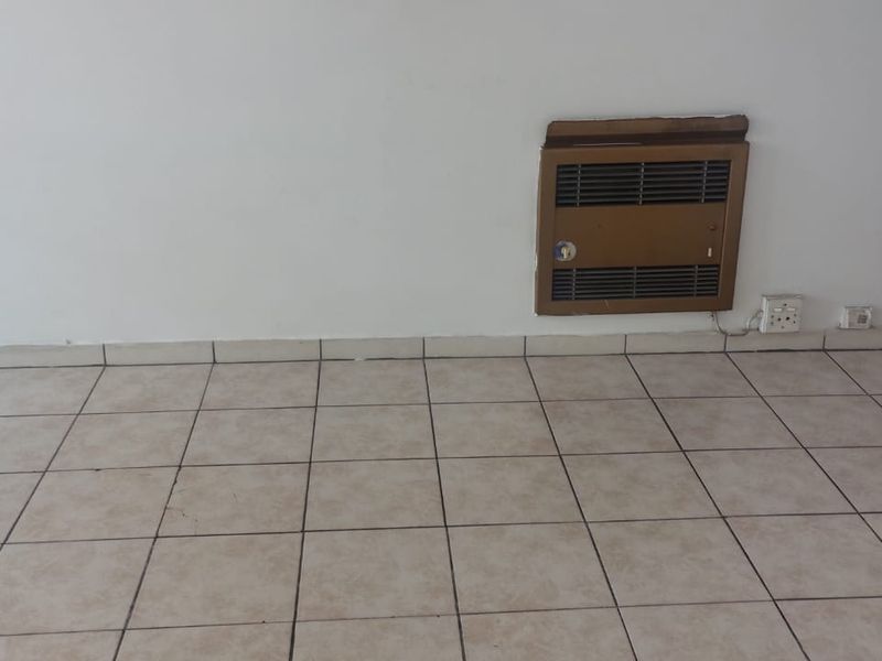 An empty living area featuring neutral tiled flooring and a built-in wall-mounted gas heater.