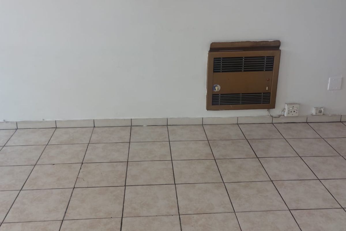 An empty living area featuring neutral tiled flooring and a built-in wall-mounted gas heater.