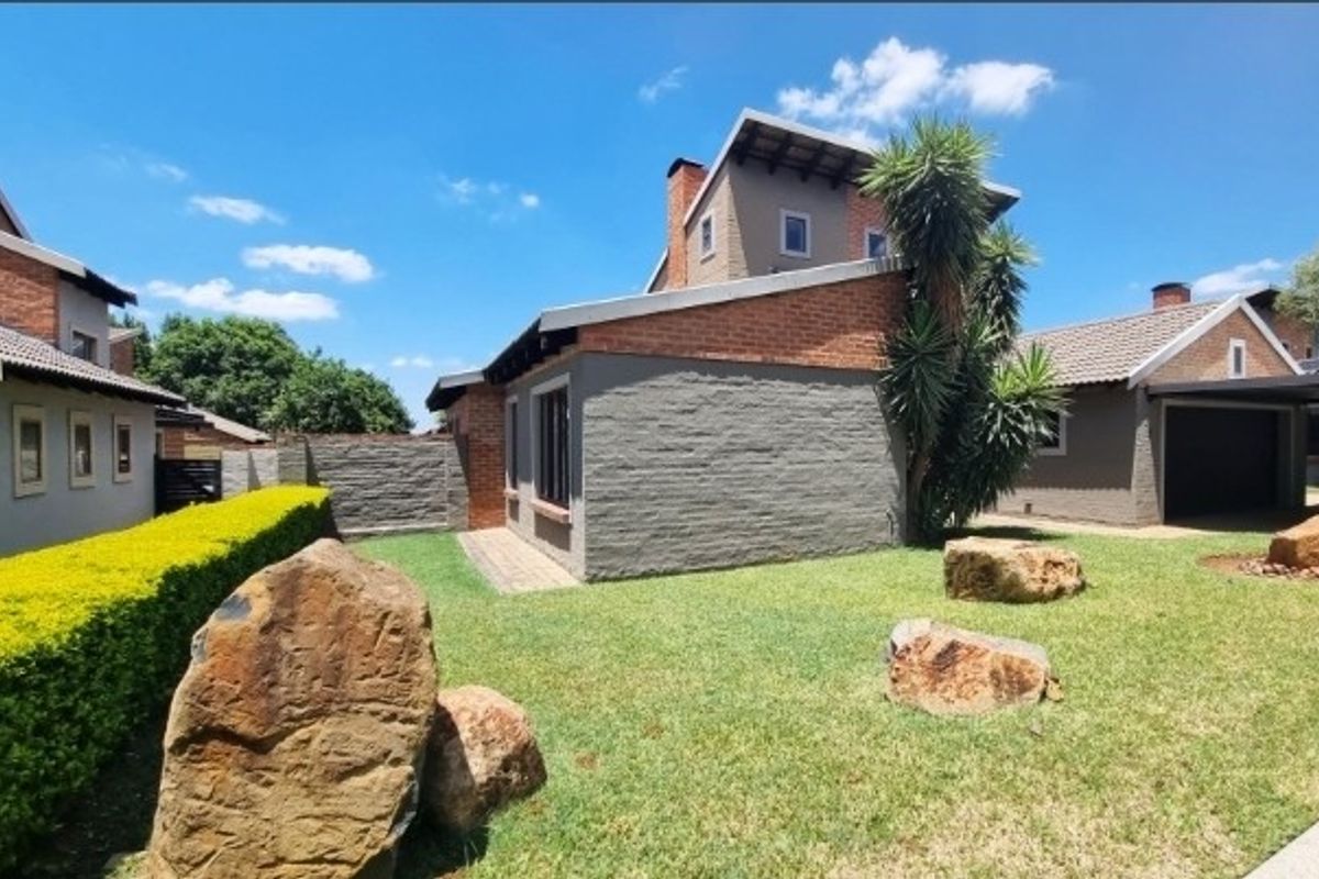 A view of the rear exterior of the house featuring a landscaped garden, brick and rendered wall finishes, and a paved walkway.