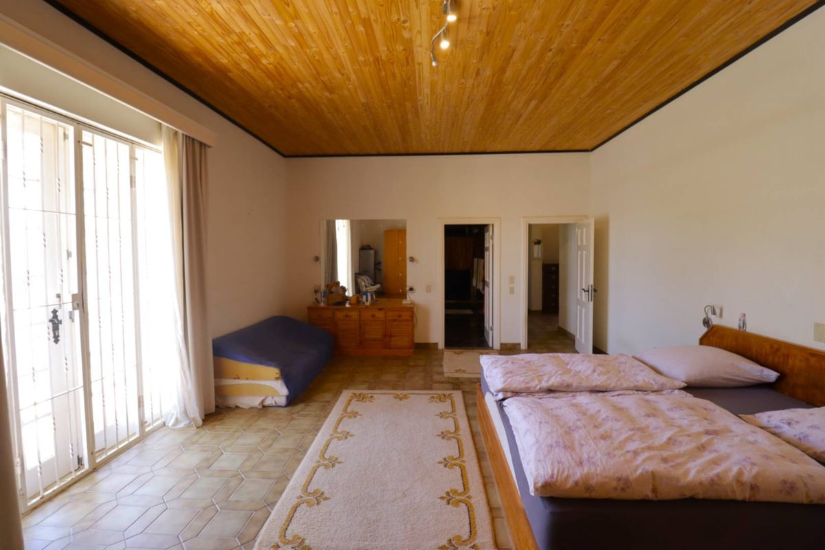 Spacious bedroom featuring a high wooden ceiling, tiled flooring, and direct access to an outdoor area through a security-gated glass door.