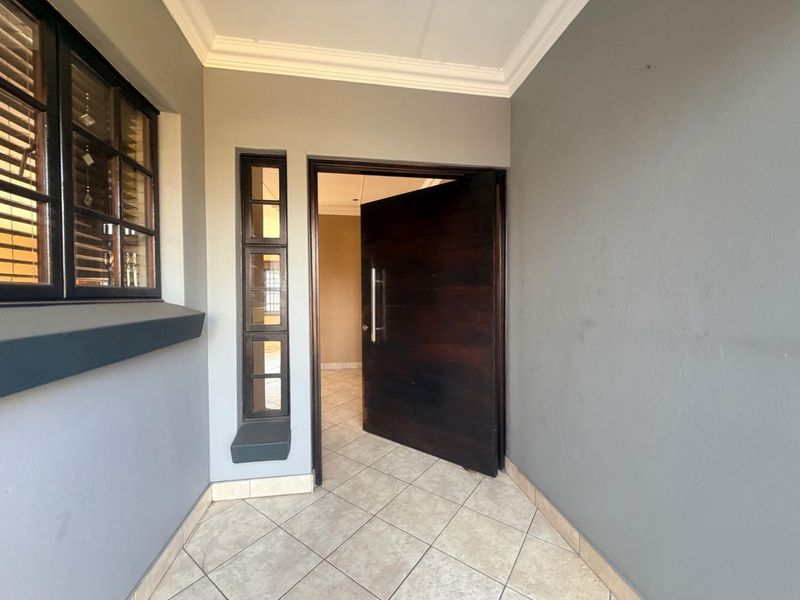 A clean and modern entrance area featuring a large solid timber pivot door, tiled flooring, and a side light window with neutral grey walls.