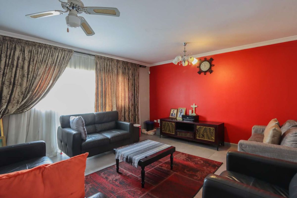 A living room featuring a bold red accent wall, tiled flooring, and a ceiling fan.