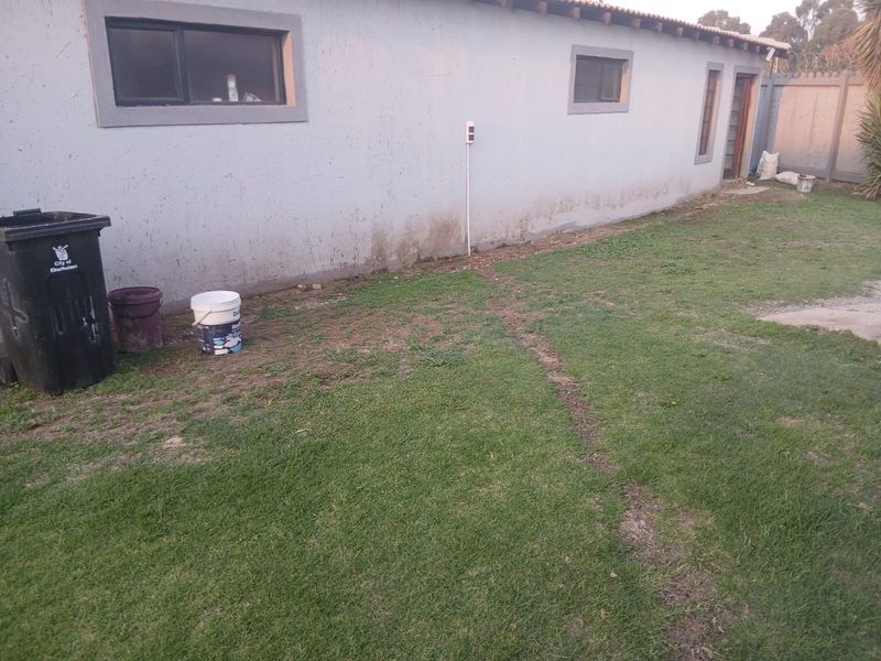 Rear exterior view of the property showing a lawn area, perimeter wall, and the back facade with visible signs of damp and wall staining.