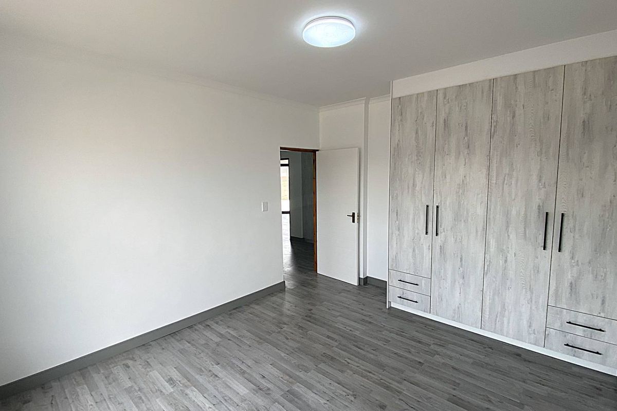 A bright, modern bedroom featuring wood-look laminate flooring and extensive built-in cabinetry with a contemporary finish.