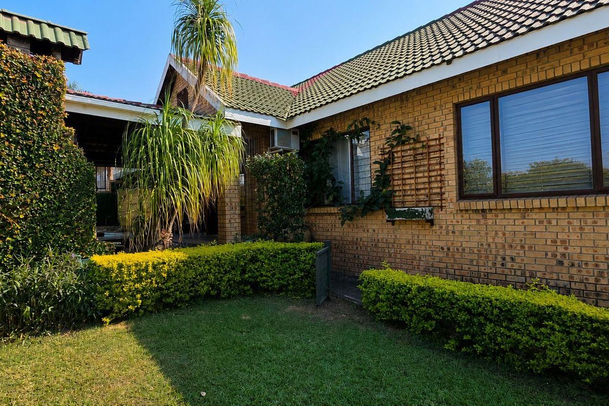 Rear view of a face brick house featuring a tiled roof, aluminium window frames, and a covered patio area with established garden.