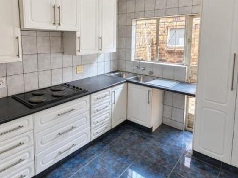 A functional kitchen featuring white built-in cabinetry, a dark countertop, electric hob, and a double sink with tiled finishes throughout.