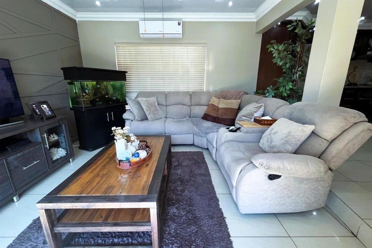 A comfortable living room featuring tiled flooring, crown molding, and a wall-mounted air conditioning unit, with an open-plan layout connecting to the kitchen area.
