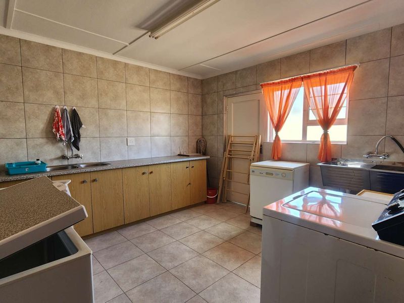 Functional laundry room featuring built-in cabinetry, laminate countertops, double stainless steel sink, and full-height wall tiling.
