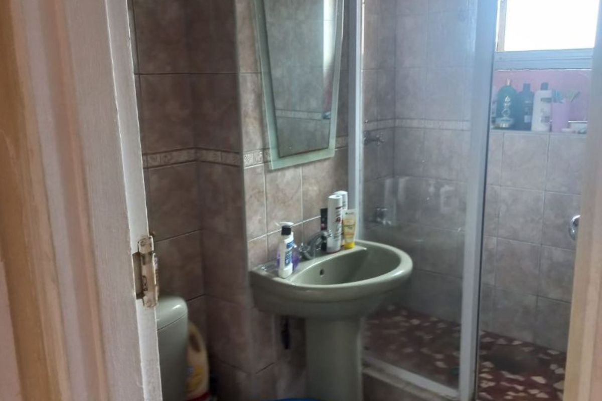 A compact bathroom featuring a pedestal basin, a shower enclosure with a glass door, and tiled walls.