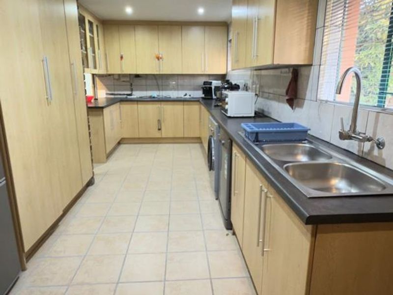 A functional kitchen featuring extensive laminate cabinetry, tiled flooring, a double bowl stainless steel sink, and ample counter space.