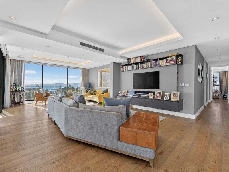 Spacious living room featuring hardwood floors, recessed ceiling lighting, ducted air conditioning, and a custom built-in media unit with expansive ocean views.