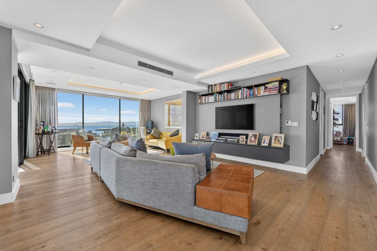 Spacious living room featuring hardwood floors, recessed ceiling lighting, ducted air conditioning, and a custom built-in media unit with expansive ocean views.
