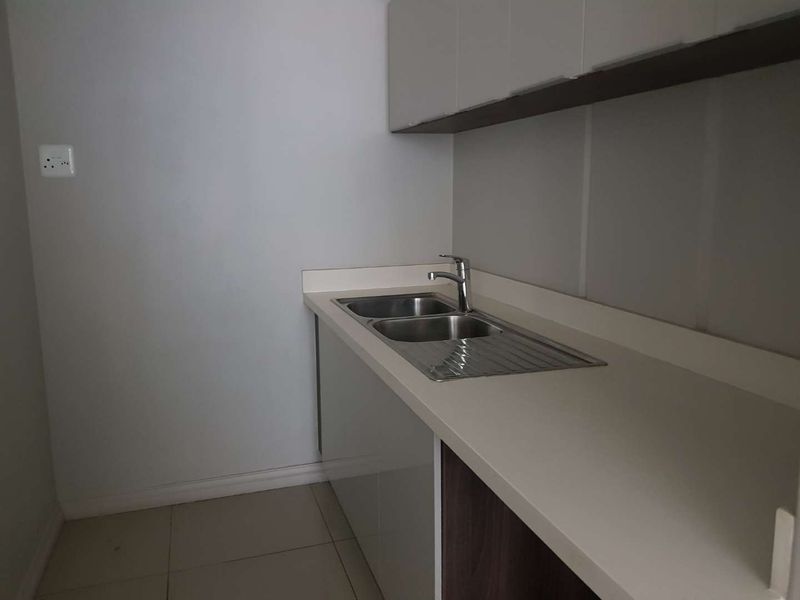 A clean and modern kitchen area featuring built-in cabinetry, a stainless steel double sink with mixer tap, and neutral tiled flooring.