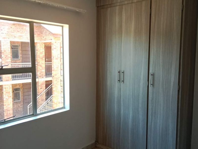 A clean, empty bedroom featuring tiled flooring, a built-in wardrobe, and an aluminium-framed window with natural light.