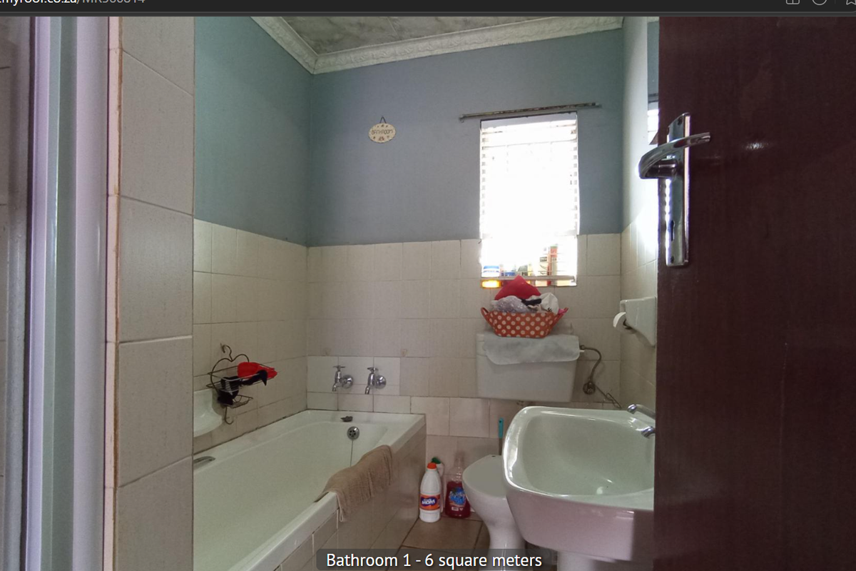 A functional bathroom featuring a built-in bathtub, pedestal basin, and toilet, with partial wall tiling and a window for natural light.