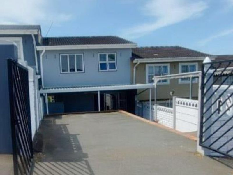 Front exterior view of the property featuring a paved driveway, secure metal gate, and a covered carport area.