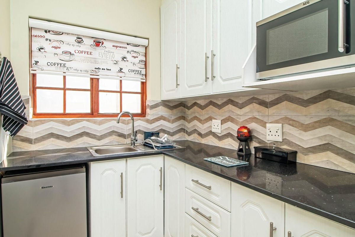 Compact kitchen featuring white cabinetry, dark granite countertops, a stainless steel sink, and a decorative chevron-patterned tiled backsplash.