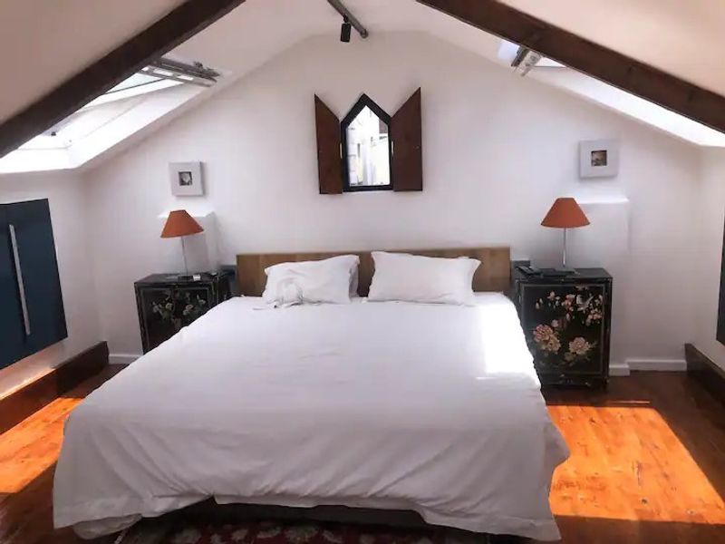 Attic bedroom featuring exposed timber beams, hardwood flooring, and dual skylight windows providing natural light.