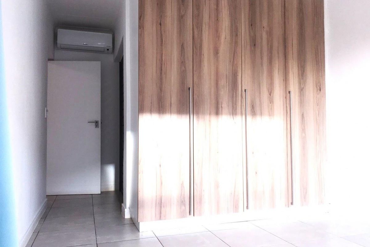 A bright bedroom featuring modern wood-grain built-in cupboards, tiled flooring, and a wall-mounted air conditioning unit.