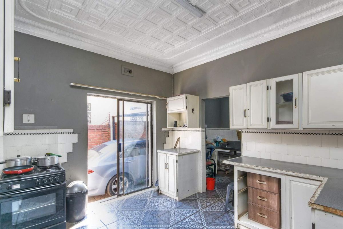 A dated kitchen featuring original cabinetry, tiled flooring, and a sliding door leading to an exterior area, offering significant potential for renovation.