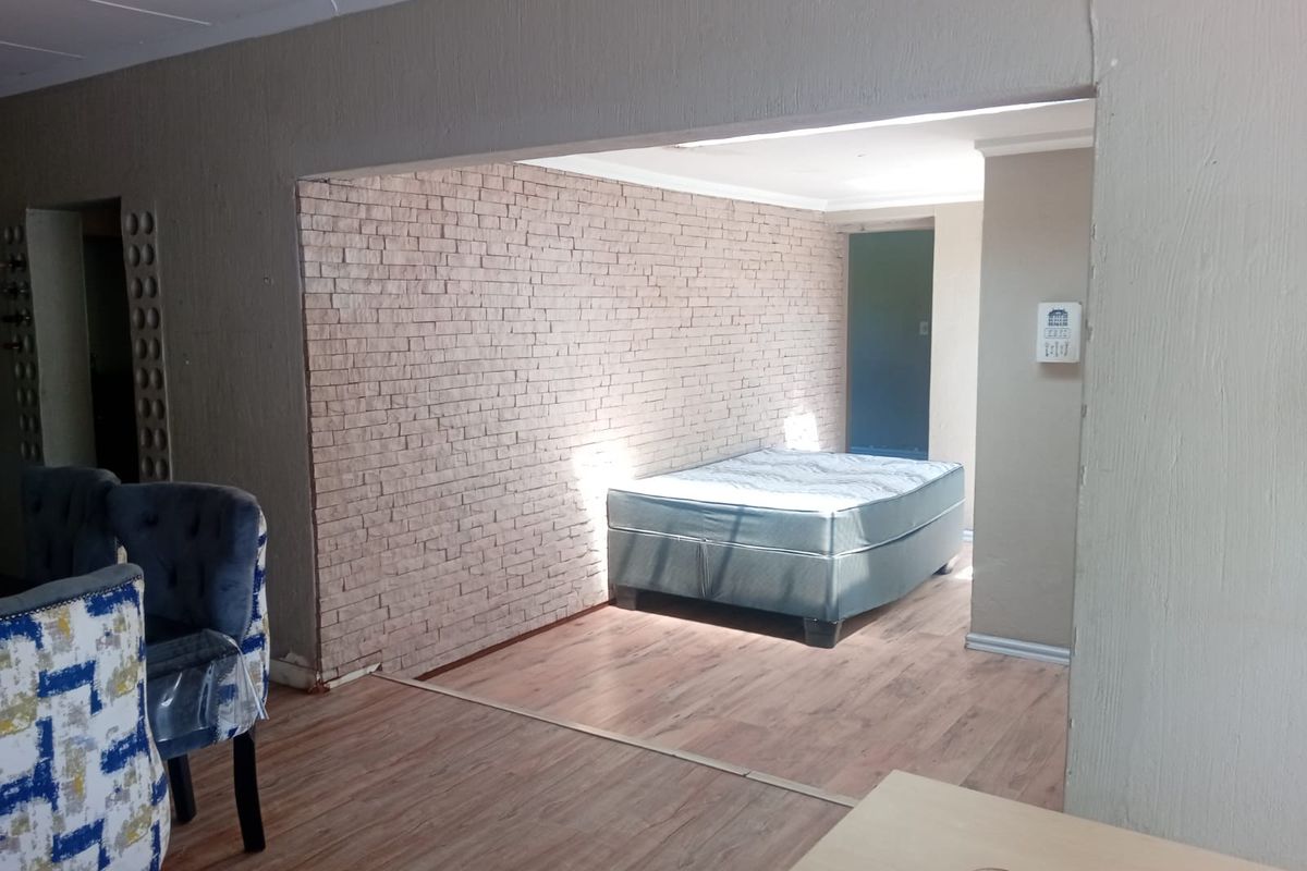 A bedroom featuring laminate flooring and a textured brick feature wall, offering a neutral canvas for interior design updates.
