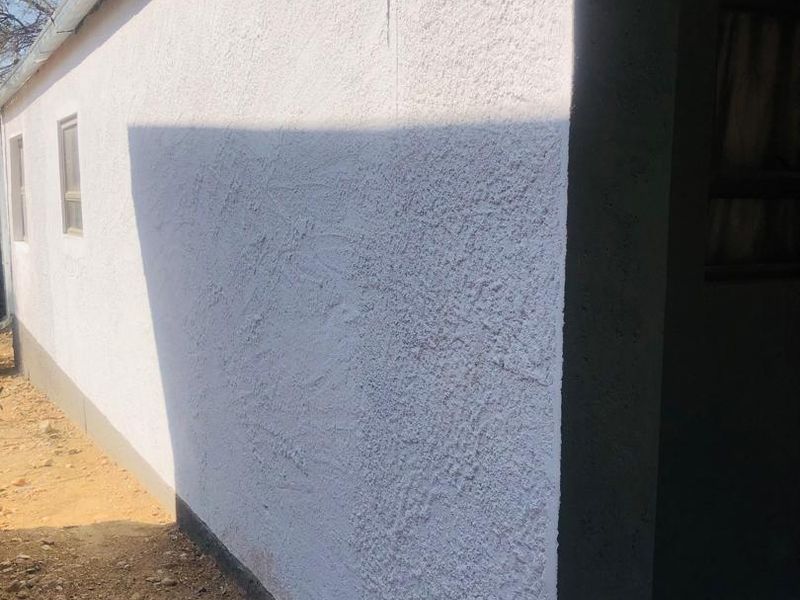 Side view of the property showing textured exterior walls, guttering, and aluminium window frames with an adjacent tiled entrance area.