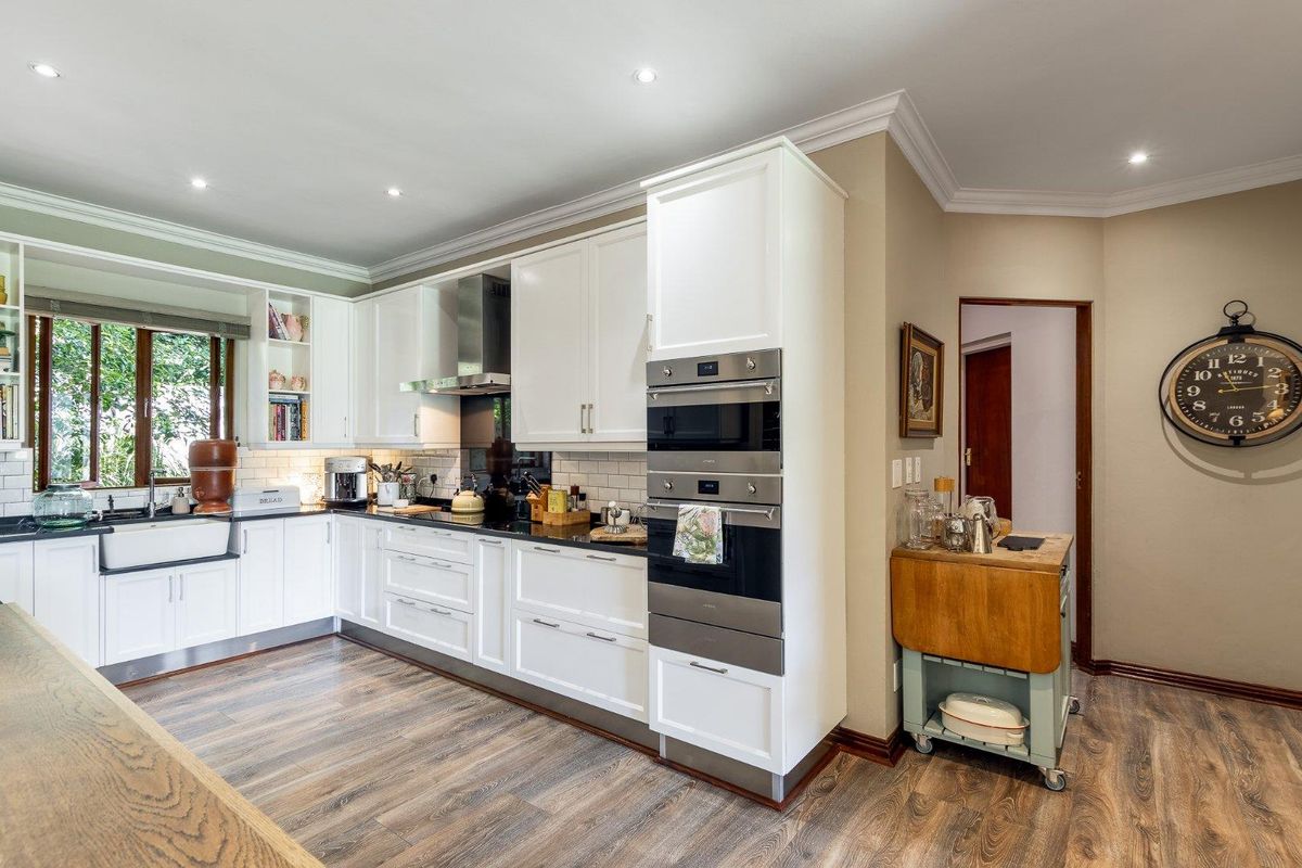 A well-appointed kitchen featuring white cabinetry, dark countertops, a farmhouse sink, built-in oven, and integrated microwave, complemented by wood-look flooring and recessed lighting.