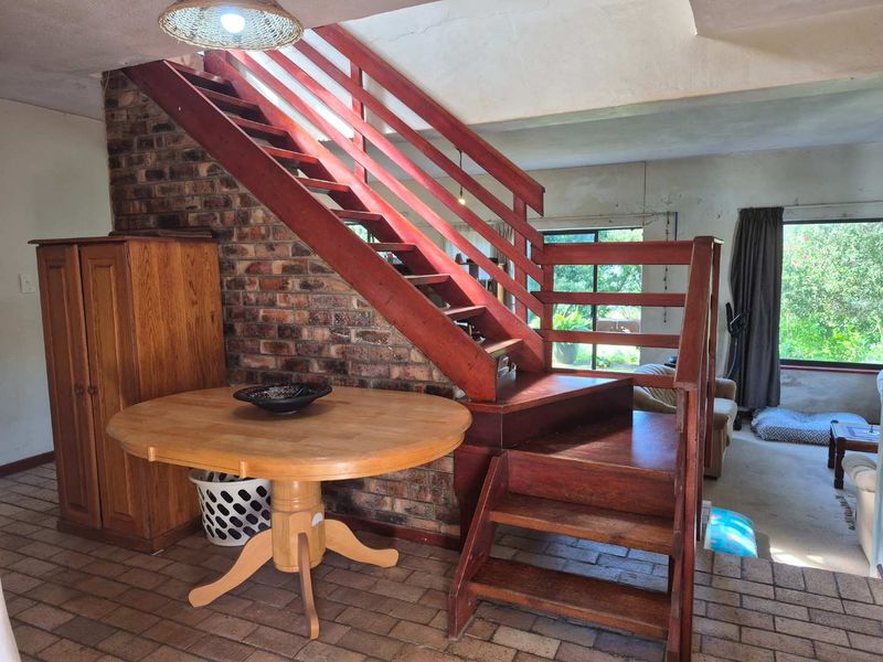 Living area featuring an exposed brick wall and a prominent timber staircase, with direct access to the garden through sliding glass doors.