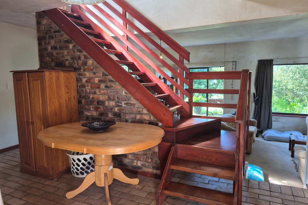 Living area featuring an exposed brick wall and a prominent timber staircase, with direct access to the garden through sliding glass doors.