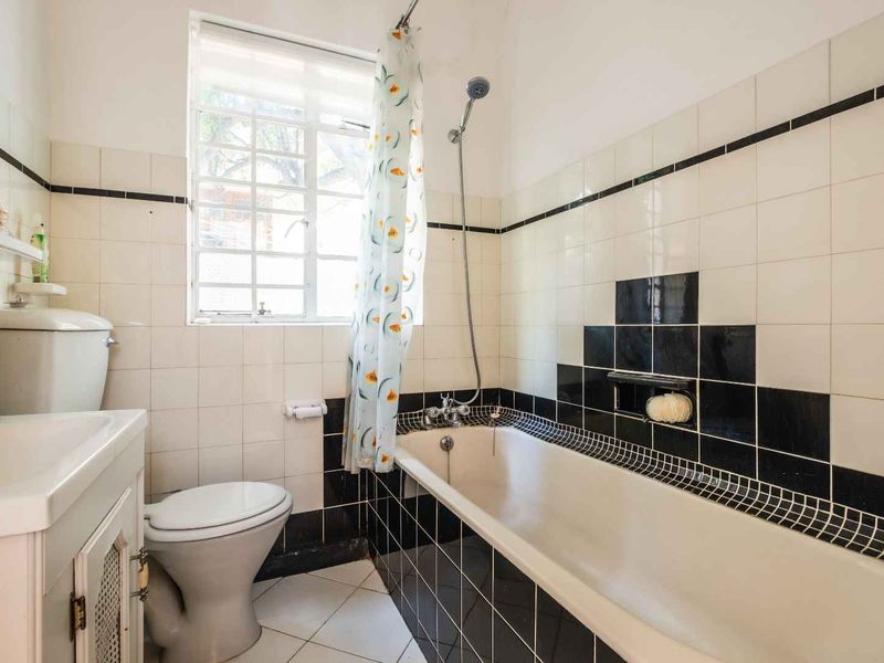 A functional bathroom featuring a bathtub with shower attachment, a vanity basin, and a toilet, finished with classic black and white wall tiling.