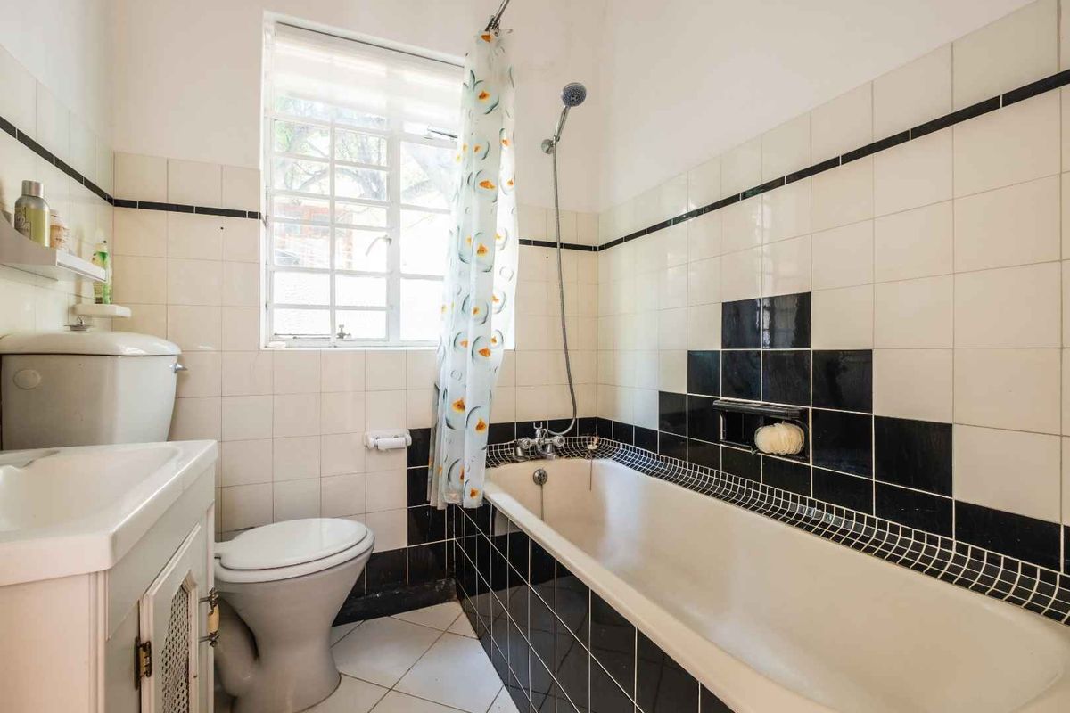 A functional bathroom featuring a bathtub with shower attachment, a vanity basin, and a toilet, finished with classic black and white wall tiling.