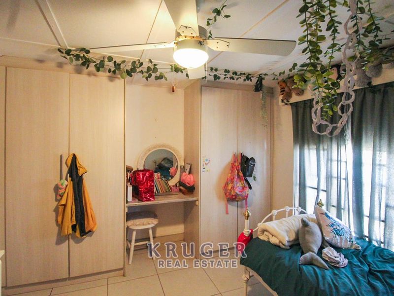 A bedroom featuring built-in cupboards, a vanity area, and a ceiling fan, finished with tiled flooring.