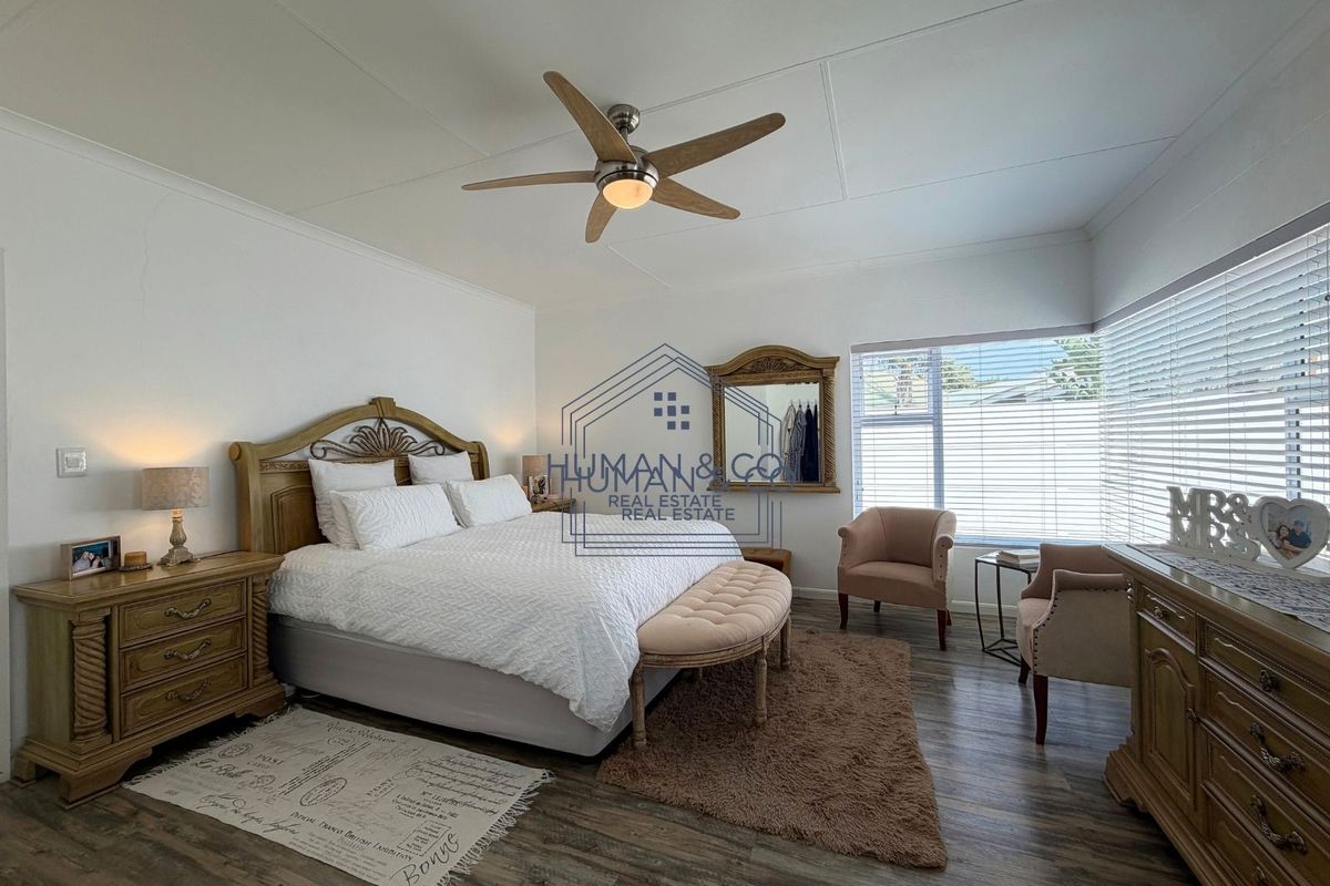 Spacious bedroom featuring laminate flooring, a ceiling fan, and large windows with venetian blinds, offering a comfortable and well-lit living space.