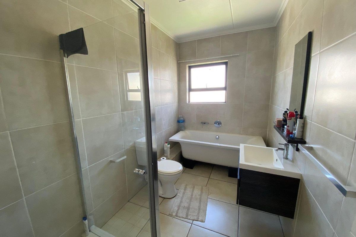 A functional bathroom featuring a glass-enclosed shower, a freestanding bathtub, a wall-mounted vanity, and neutral floor-to-ceiling tiling.