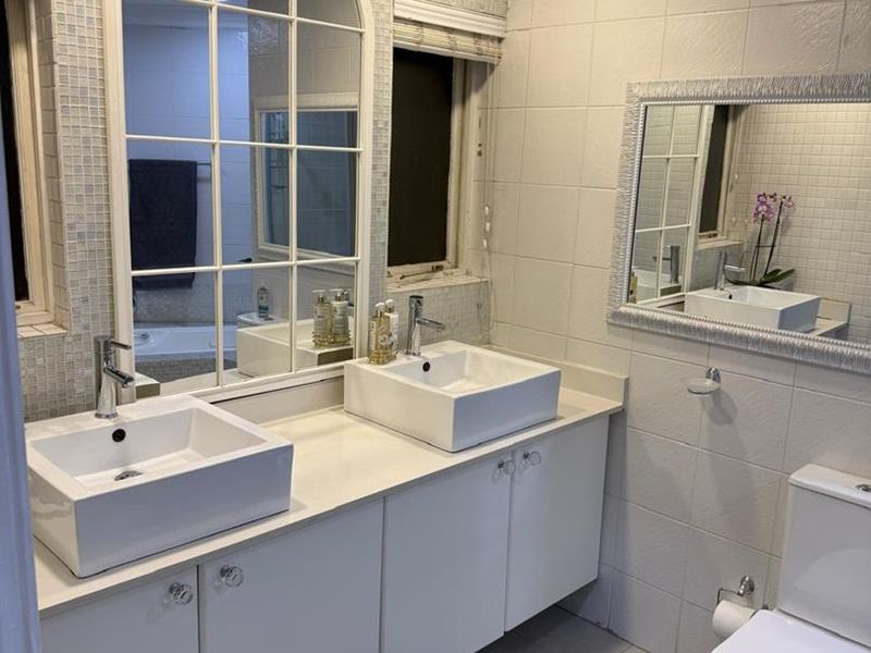 A well-maintained bathroom featuring a double vanity with vessel sinks, tiled walls, and modern fixtures.