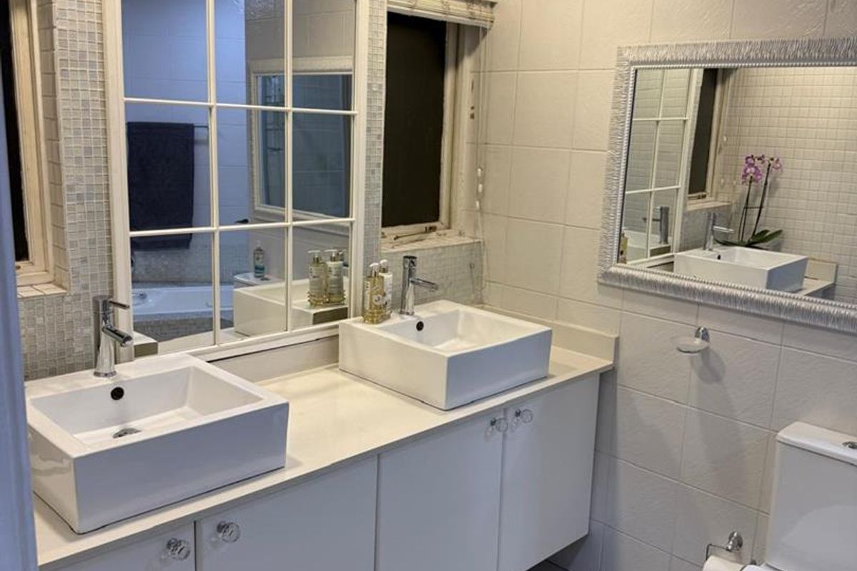 A well-maintained bathroom featuring a double vanity with vessel sinks, tiled walls, and modern fixtures.