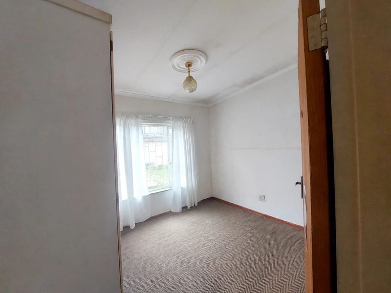 An empty bedroom featuring carpeted flooring, a decorative ceiling rose, and a window fitted with security bars.