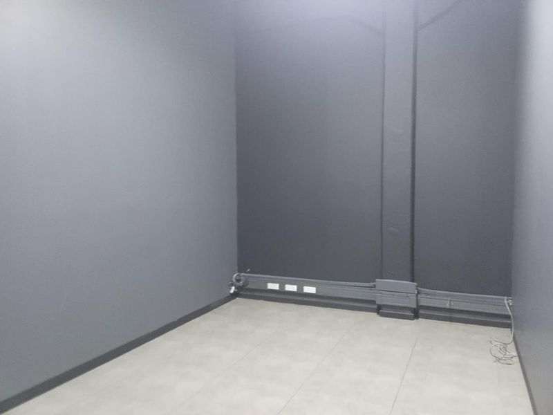 An empty office space featuring dark grey painted walls, tiled flooring, and surface-mounted electrical trunking with integrated power outlets.