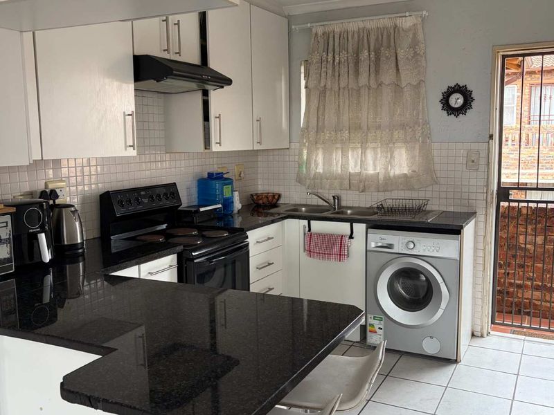 Functional kitchen featuring granite countertops, white cabinetry, tiled backsplash, and integrated space for a washing machine with direct access to the exterior.