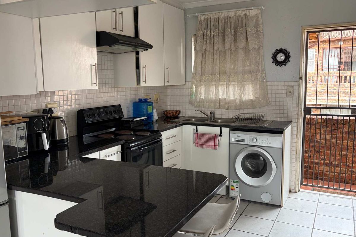 Functional kitchen featuring granite countertops, white cabinetry, tiled backsplash, and integrated space for a washing machine with direct access to the exterior.